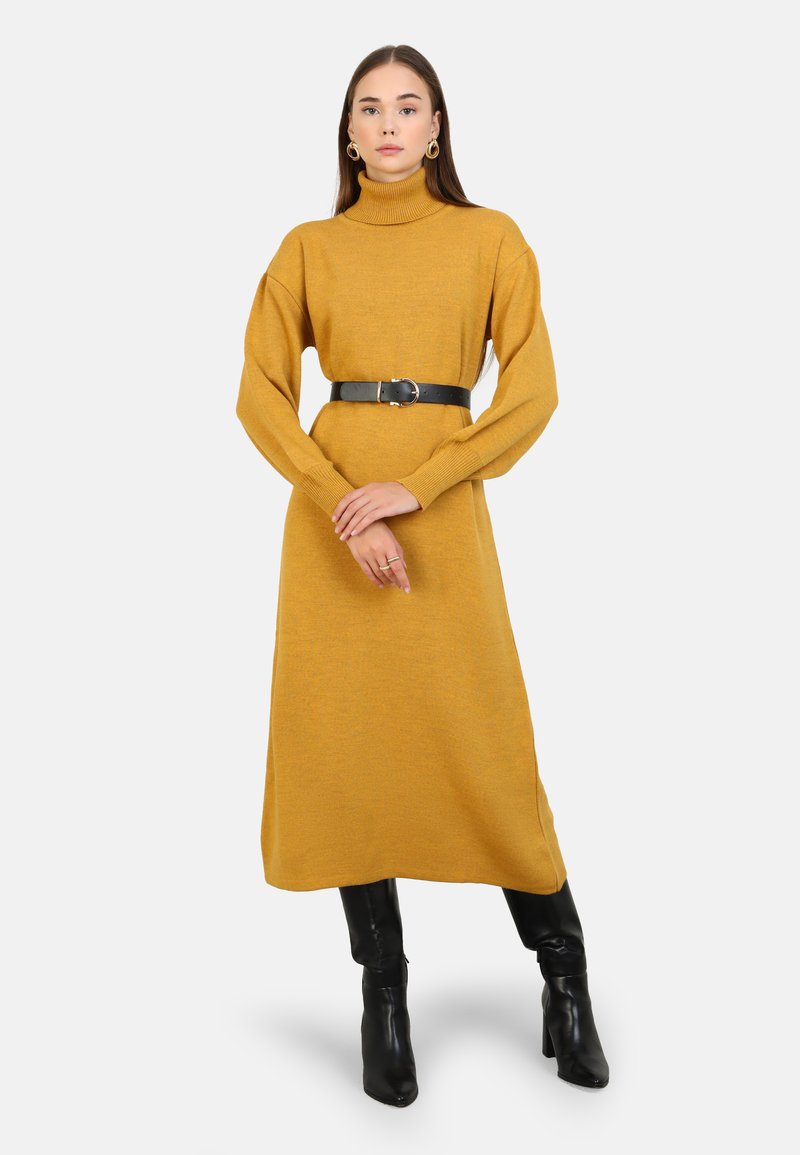Abito turtleneck giallo senape con maniche lunghe e cintura nera. L'abito è di lunghezza media e presenta un design a maglia texture. Stivali neri fino al ginocchio.