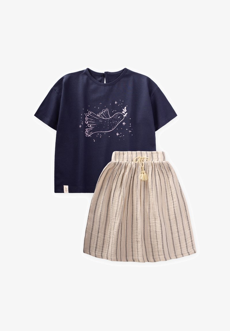 Jūreivio spalvos medvilnės marškinėliai su balta paukščio grafika, derinami su smėlio spalvos dryžuota sijonu, turinčiu elastinę juostą ir kutą.