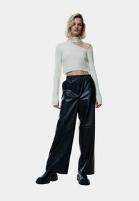 Witte cropped trui met een hoge hals en asymmetrische snit, gecombineerd met hoge zwarte neplederen wijde broek en stevige zwarte laarzen.
