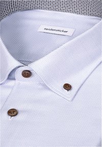 Chemise habillée bleu clair texturée avec des boutons marron et une étiquette portant la mention "seidensticker" à l'intérieur du col.