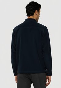 Tmavě modrá košile s límečkem, knoflíkovými manžetami a texturovanou látkou. Vhodná pro vrstvené outfity.