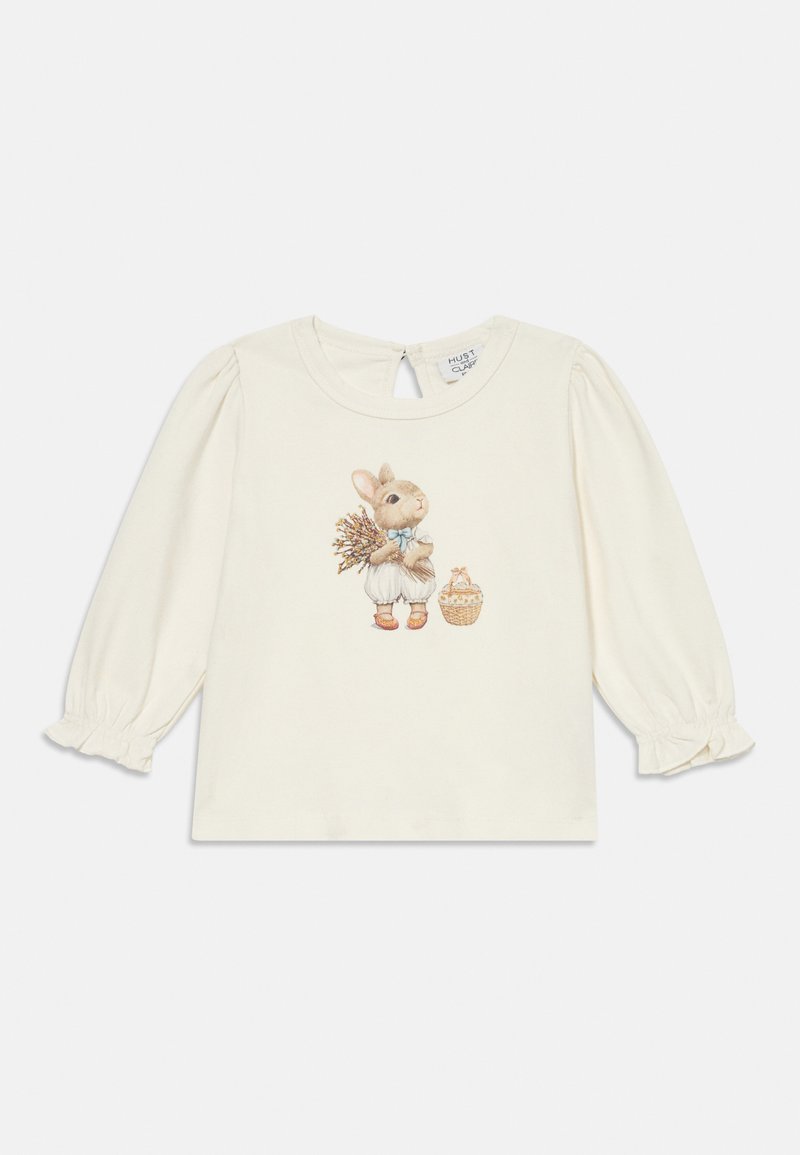 Cremfarbene Langarmbluse mit elastischen Bündchen, verziert mit einem gestickten Hasen, der Blumen und einen Korb hält. Mit Schlüssellochverschluss hinten.