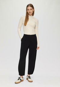 Gestreepte langemouwen top in crème en beige; hoge taille zwarte broek met een relaxte fit; twee-kleurige sneakers met veters en een rubberen zool.