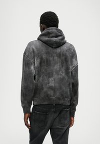 Γκρι φούτερ με υφή και ξεθωριασμένο φινίρισμα. Διαθέτει κουκούλα, κρεμαστούς ώμους και ραμμένα μανίκια. Συνδυάζεται με σκούρα τζιν.