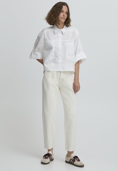 Chemise blanche courte avec fermeture à boutons, deux poches avant et manches retroussées. Associée à un jean droit écru et des baskets multicolores.