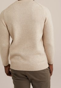 Beige pletený svetr s texturovaným povrchem, ribbovaný lem a manžety, s raglánovými rukávy. Spárován s olivově zelenými kalhotami.