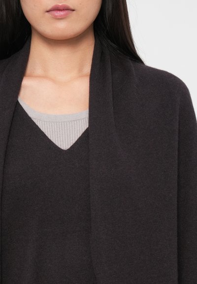 Gilet en tricot gris foncé avec une texture douce, ouvert à l'avant, et un top en côte gris clair à col en V en dessous. Accent sur le contraste des tissus et des couleurs.