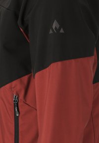 Röd och svart utomhusjacka med en ficka med dragkedja och en triangulär logotyp på ärmen. Tillverkad av ett slitstarkt och slätt material.