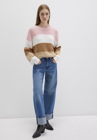 Gestrickter Pullover mit rosa, weißen und braunen Streifen; kombiniert mit hoch taillierten, hellblauen Jeans mit umgeschlagenen Bündchen und schwarzen Stiefeln mit Absatz.