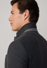 Cappotto in misto lana grigio scuro con colletto alto, caratterizzato da un accento grigio più chiaro sul bordo del colletto e una trama liscia.