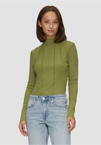 Pull à col roulé vert olive à manches longues avec des détails de couture verticaux. Tissu léger et texturé associé à un jean en denim bleu clair.