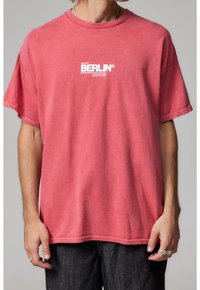 Czerwona bawełniana koszulka w luźnym kroju, z okrągłym dekoltem i krótkimi rękawami. Na przodzie znajduje się graficzny napis "Berlin" oraz "2009."