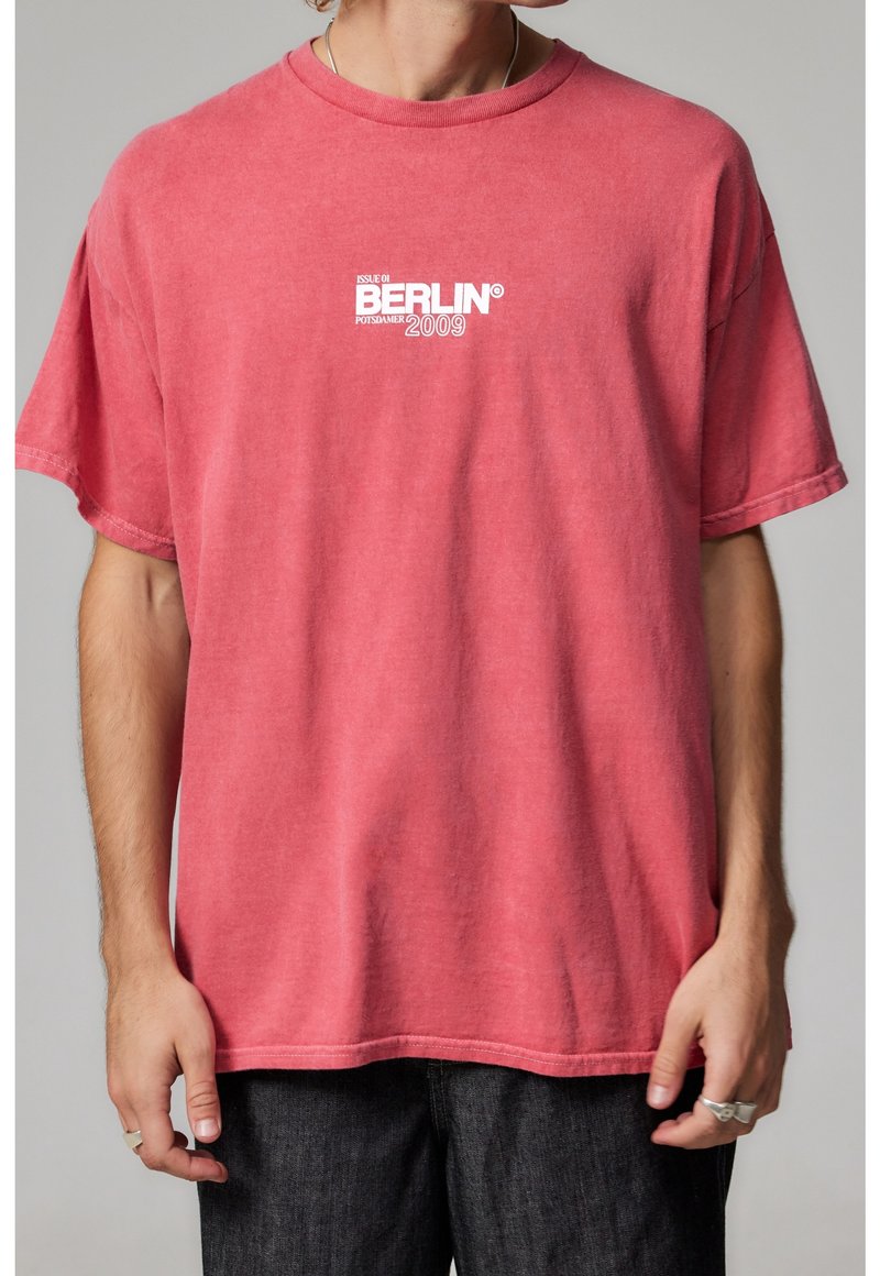 Czerwona bawełniana koszulka w luźnym kroju, z okrągłym dekoltem i krótkimi rękawami. Na przodzie znajduje się graficzny napis "Berlin" oraz "2009."