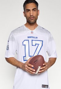 Balts NFL kreklā ar zilām detaļām, uz kura rakstīts "BUFFALO" un skaitlis "17". Spēlētājs tur brūnu futbolbola bumbu, redzama roku tekstūra.