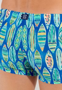Badehose mit blauem Hintergrund und bunten Blattmustern in Grün, Gelb und Rot, aus einem glatten, leichten Stoff gefertigt.
