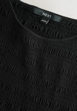 Melns tops ar teksturētu, savākto dizainu. Raksturo apaļu kakla izgriezumu un uzlīmi ar uzrakstu "NEXT". Izgatavots no mīksta, elastīga auduma.