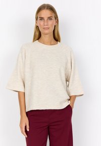 Beżowy sweter dziany, krótki rękaw, okrągły dekolt i luźny krój, zestawiony z burgundowymi spodniami. Gładka faktura, subtelne wariacje kolorystyczne.