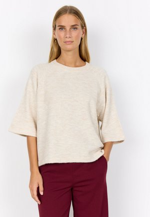Beige gebreide trui met korte mouwen, ronde halslijn en een ontspannen pasvorm, gecombineerd met bordeauxrode broek. Glad textuur, subtiele kleurvariaties.