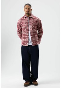 Rood-wit geruit flanellen overhemd met knoopsluiting, gedragen over een wit T-shirt, gecombineerd met donkerblauwe wijd uitlopende broek en bruine schoenen.