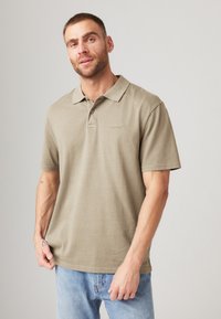 Lys beige polo skjorte med krage, korte ermer og en diskret logo. Laget av bomull med en myk, glatt tekstur. Brukt sammen med denim jeans.