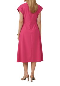 Roze midi-jurk met kapmouwen, een aansluitend lijfje en een uitlopende rok. Gladde textuur, achternaden zichtbaar, gepaard met beige hakken sandalen.