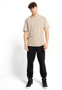 Krótki rękaw, tanowy t-shirt zestawiony z czarnymi spodniami dresowymi i czarnymi trampkami za kostkę. Prosty design z luźnym krojem i miękką fakturą.
