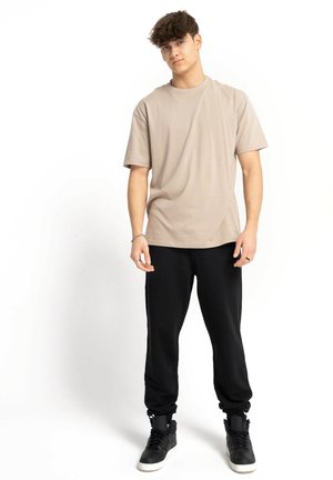 Krótki rękaw, tanowy t-shirt zestawiony z czarnymi spodniami dresowymi i czarnymi trampkami za kostkę. Prosty design z luźnym krojem i miękką fakturą.