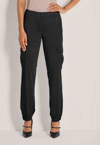Schwarze Cargo-Hosen mit seitlichen Taschen und elastischen Bündchen, aus einem glatten Stoff gefertigt. Kombiniert mit schwarzen High Heels für einen Kontrast.