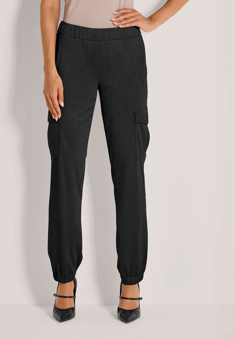 Schwarze Cargo-Hosen mit seitlichen Taschen und elastischen Bündchen, aus einem glatten Stoff gefertigt. Kombiniert mit schwarzen High Heels für einen Kontrast.