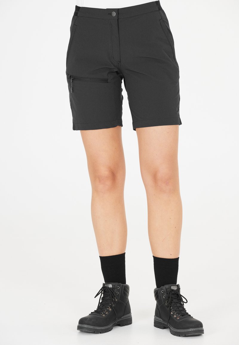 Svarta knä-långa shorts i mjukt, stretchigt tyg med en sidoficka med dragkedja; tillsammans med svarta stövlar och mörka strumpor.