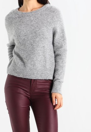 Pull gris en maille avec un col rond et des manches longues, associé à un pantalon en cuir bordeaux. Texture douce et coupe légèrement ample.