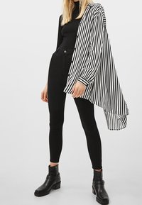 Czarna i biała, w paski, oversize'owa koszula, teksturowana tkanina, zapinana na guziki, w połączeniu z czarnymi, obcisłymi dżinsami i botkami za kostkę.