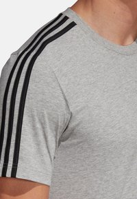 T-shirt grigio con una texture morbida, caratterizzato da tre strisce nere sulle spalle e un classico collo rotondo.