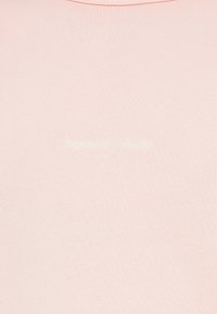 Tela rosa claro con texto bordado sutil en blanco que dice "Originals Studio" en cursiva.