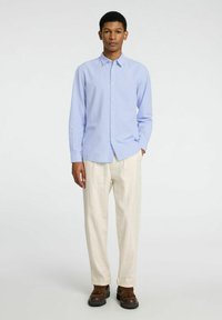 Camicia azzurra chiara con colletto, maniche lunghe e vestibilità comoda, abbinata a pantaloni color crema e scarpe marroni.