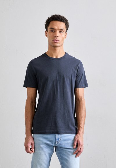 Tricou din bumbac gri închis, cu decolteu rotund și mâneci scurte, purtat cu blugi albaștri deschiși. Textură netedă, fără modele vizibile.