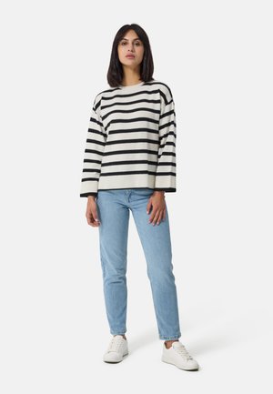Gestreifter Pullover in Creme und Schwarz, weite Ärmel, lockere Passform. Kombiniert mit hellblauen Jeans und weißen Sneakern. Einfache, legere Gestaltung.