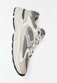 Baskets de sport grises et beiges avec lacets blancs, empeigne en mesh et en daim, semelle blanche épaisse et crampons noirs, présentées sur fond blanc.