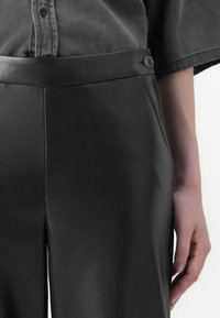 Zwarte faux leather broek met een gladde textuur, voorzien van een knoopsluiting bij de tailleband en zijzakken.
