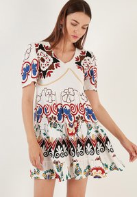 Short-sleeved white dress with colorful floral and swirl patterns, a V-neckline, and flared skirt. Features decorative stitching and accents.