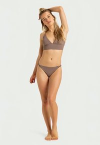 Ensemble de bikini marron comprenant un haut bralette triangulaire et un bas de bikini taille basse, fabriqué dans un tissu lisse et extensible avec des coutures minimales.