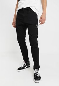 Pantalones cargo negros con un corte ajustado que presentan bolsillos frontales, cremalleras y un acento de bucle lateral. Combinados con zapatillas altas negras.