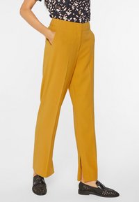 Pantalones rectos de color mostaza con bolsillos laterales y detalle de dobladillo dividido. Tejido suave, diseño ajustado y cinturilla de altura media.