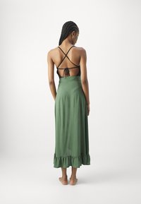 Gonna maxi verde con orlo a balze abbinata a un top nero con incrocio sulla schiena, che mostra una texture liscia e un design minimalista.