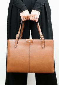 Bruine leren schoudertas met een gladde textuur, twee verstelbare handvatten en een magnetische sluiting aan de voorkant. Eenvoudig, rechthoekig ontwerp.