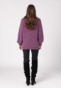 Maglione viola con texture e maniche a palloncino, abbinato a jeans neri slim e stivali neri con tacco al ginocchio. Vista da dietro.