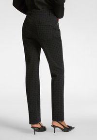 Jeans negros con estampado y corte recto, que cuentan con dos bolsillos traseros, y combinados con zapatos de tacón negros.