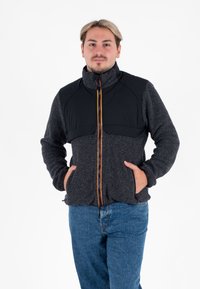 Donkergrijze fleecejas met een zwart, gevoerd bovenstuk. Voorzien van een voorkant rits met oranje details en twee zijvakjes.