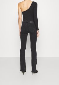 Top negro de un solo hombro con manga larga, combinado con jeans de mezclilla oscuros de talle alto y con campana. Textura suave, detalles mínimos, sin elementos de marca visibles.