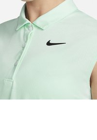 Chemise sans manches vert clair avec col, trois boutons et logo Nike swoosh noir près de l'épaule droite.